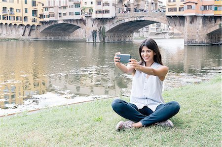 simsearch:649-08306717,k - Young woman sitting on riverbank in front of Ponte Vecchio and Arno river using smartphone to take selfie, Florence, Tuscany, Italy Photographie de stock - Premium Libres de Droits, Code: 649-08306730