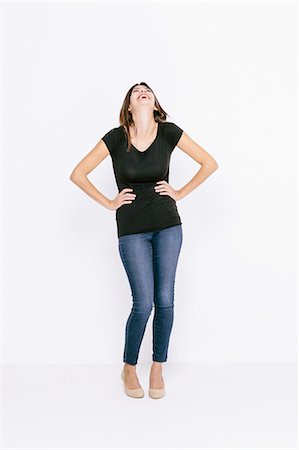 Full length front view of young woman, hands on hips, head back laughing Stock Photo - Premium Royalty-Free, Code: 649-08306743