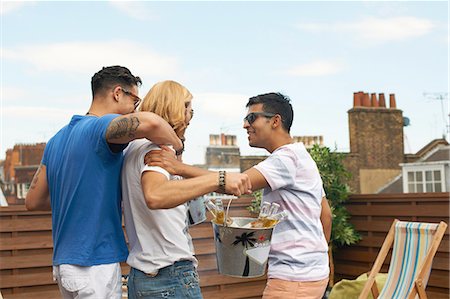 simsearch:614-05792406,k - Three male friends carrying ice bucket with bottled beer at rooftop party Fotografie stock - Premium Royalty-Free, Codice: 649-08306805