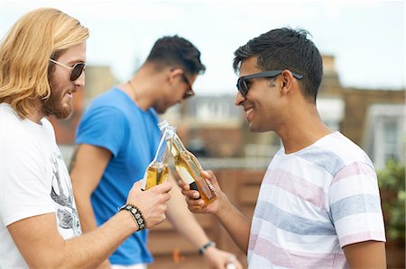 sharing a drink - Two male friends making a toast with bottled beer at rooftop party Stock Photo - Premium Royalty-Free, Code: 649-08306806