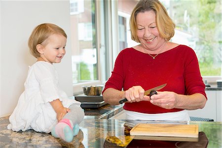 simsearch:614-08535822,k - Female toddler sitting on kitchen counter watching grandmother Stock Photo - Premium Royalty-Free, Code: 649-08307449