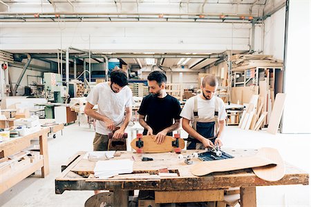 simsearch:649-08329135,k - Front view of young men in carpentry workshop standing at workbench attaching wheels to skateboard Foto de stock - Royalty Free Premium, Número: 649-08327870