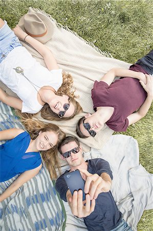 simsearch:649-08328214,k - Group of young adults lying on picnic blankets, taking self portrait using smartphone Foto de stock - Royalty Free Premium, Número: 649-08328218