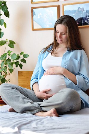 Pregnant woman sitting on bed, holding stomach Foto de stock - Sin royalties Premium, Código: 649-08328511