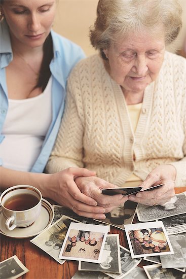 Senior woman and granddaughter sitting at table, looking through old photographs Stock Photo - Premium Royalty-Free, Image code: 649-08328529