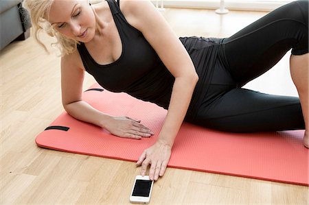 Cropped view of mature woman lying on side on yoga mat looking down using smartphone Stock Photo - Premium Royalty-Free, Code: 649-08328825