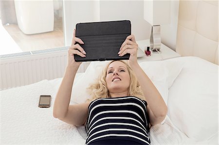 simsearch:649-08328825,k - High angle view of mature woman lying on back on bed, arms raised holding digital tablet Foto de stock - Sin royalties Premium, Código: 649-08328823