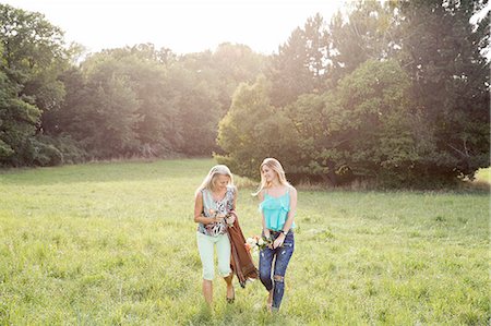 simsearch:649-08381348,k - Front view of women carrying picnic blanket and flowers walking on field landscape smiling Fotografie stock - Premium Royalty-Free, Codice: 649-08328843