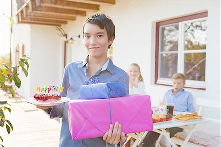 porte de la terasse - Portrait of teenage boy carrying birthday cake and birthday gifts on patio Foto de stock - Sin royalties Premium, Código: 649-08381234