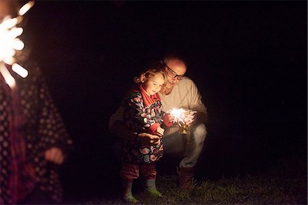 Father crouching next to daughter holding sparkler Stock Photo - Premium Royalty-Free, Code: 649-08381542