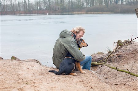 Mature man hugging dog on riverbank Foto de stock - Royalty Free Premium, Número: 649-08381685