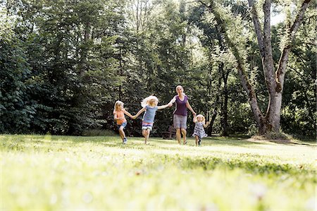 Mid adult woman and three young daughters holding hands and running in park Photographie de stock - Premium Libres de Droits, Code: 649-08422516