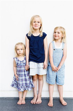 Portrait of three young sisters standing in front of white wall Stock Photo - Premium Royalty-Free, Code: 649-08422547