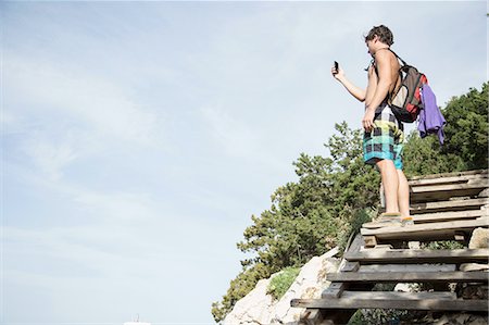 simsearch:649-08422664,k - Low angle side view of young man standing on wooden steps using smartphone to take photograph, Cala Luna, Sardinia, Italy Foto de stock - Sin royalties Premium, Código: 649-08422657