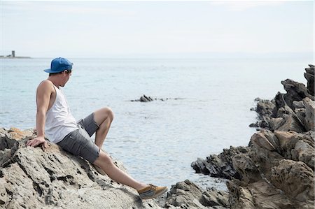 Full length side view of young man sitting on rocks looking away at ocean, Stintino, Sardinia, Italy Stockbilder - Premium RF Lizenzfrei, Bildnummer: 649-08422653