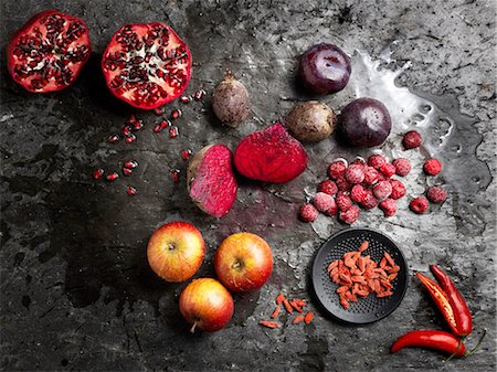 punica granatum - Overhead view of halved red fruit and vegetables on dark background Stock Photo - Premium Royalty-Free, Code: 649-08422900