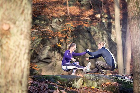 Side view of couple on rocks in forest face to face, holding hands, squatting balancing on one leg Stock Photo - Premium Royalty-Free, Code: 649-08423340