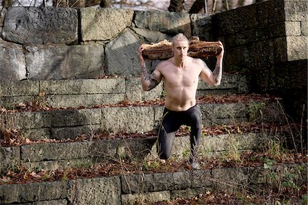simsearch:649-06164827,k - Tattooed mid adult man carrying tree branch on shoulders doing lunges on stone steps Foto de stock - Sin royalties Premium, Código: 649-08423364