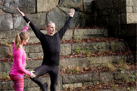 simsearch:649-08423361,k - Mid adult man on stone steps arms raised standing on one leg, young woman helping Stock Photo - Premium Royalty-Free, Code: 649-08423360