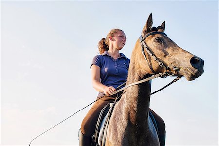 Low angle view of woman riding bay horse against blue sky Photographie de stock - Premium Libres de Droits, Code: 649-08423435