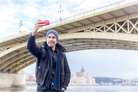 simsearch:649-08306728,k - Low angle view of young man in front of Margaret bridge using smartphone to take selfie smiling, Budapest, Hungary Foto de stock - Sin royalties Premium, Código: 649-08479370
