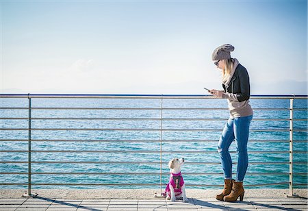 simsearch:649-08118581,k - Full length side view of young woman with dog by railings in front of ocean using smartphone Photographie de stock - Premium Libres de Droits, Code: 649-08479387