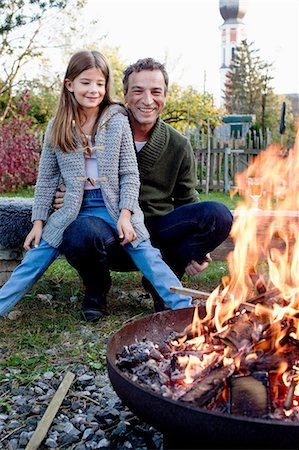 simsearch:649-08479444,k - Girl sitting on father's lap in garden watching fire pit Photographie de stock - Premium Libres de Droits, Code: 649-08479445