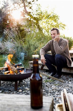 firepit and outdoors - Mature man sitting by fire pit with beer, relaxing Foto de stock - Sin royalties Premium, Código: 649-08479448