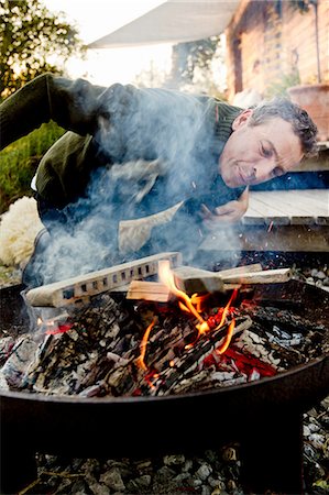 fire (things burning uncontrolled) - Mature man leaning to inspect fire pit Stock Photo - Premium Royalty-Free, Code: 649-08479443