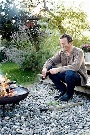 firepit and outdoors - Mature man sitting by fire pit with beer, relaxing Stock Photo - Premium Royalty-Free, Code: 649-08479534