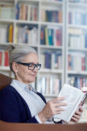 Grey haired mature woman reading book from bookshelves Stock Photo - Premium Royalty-Free, Code: 649-08479797