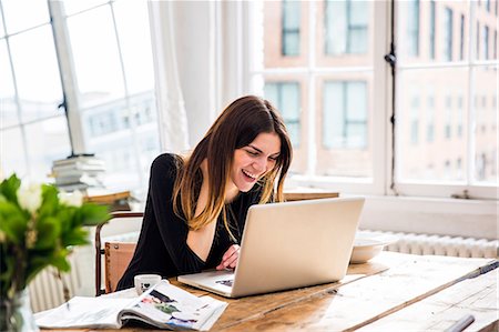 Young woman in city apartment laughing whilst working on laptop Stock Photo - Premium Royalty-Free, Code: 649-08544174