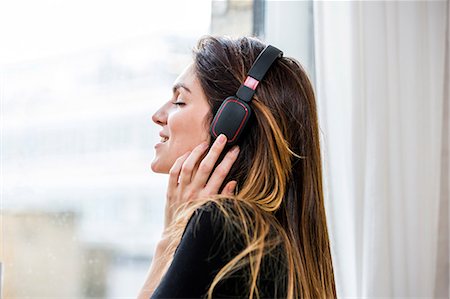 simsearch:649-08544187,k - Young woman with eyes closed listening to headphone music in front of  apartment window Foto de stock - Sin royalties Premium, Código: 649-08544180