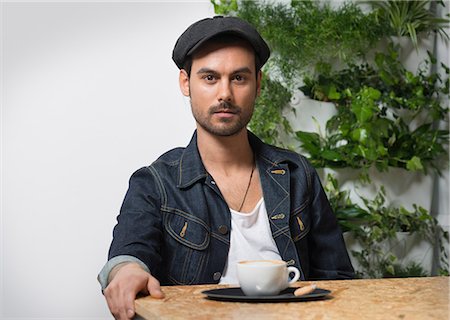 Portrait of young male hipster sitting on cafe table with coffee cup Stock Photo - Premium Royalty-Free, Code: 649-08544199