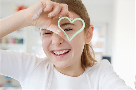 Girl looking through heart shaped cookie cutter smiling Stock Photo - Premium Royalty-Free, Code: 649-08548039