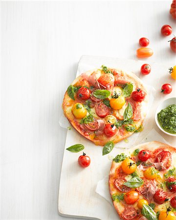 pizza white background overhead - High angle view of tomato, basil and prosciutto pizzas on cutting board Stock Photo - Premium Royalty-Free, Code: 649-08548241