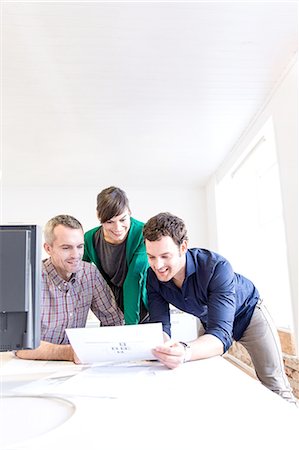 Colleagues at desk in office discussing paperwork smiling Stock Photo - Premium Royalty-Free, Code: 649-08548441