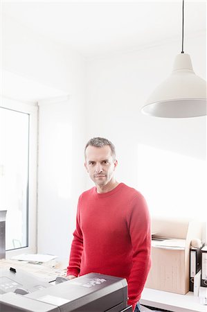 Mature man in office wearing red sweater looking at camera smiling Stock Photo - Premium Royalty-Free, Code: 649-08548486