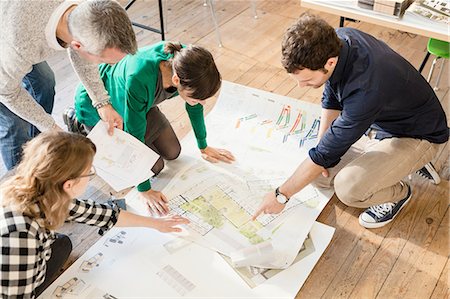 High angle view of architects discussing blueprints on wooden floor Stock Photo - Premium Royalty-Free, Code: 649-08548483