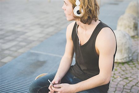 simsearch:6108-06167284,k - Young man sitting at sidewalk listening to headphone music Foto de stock - Sin royalties Premium, Código: 649-08548928
