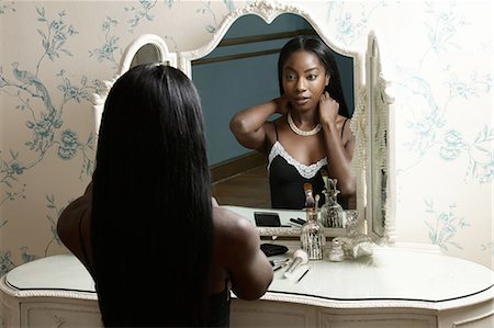Young woman sitting at dressing table, putting on necklace Foto de stock - Sin royalties Premium, Código: 649-08549080