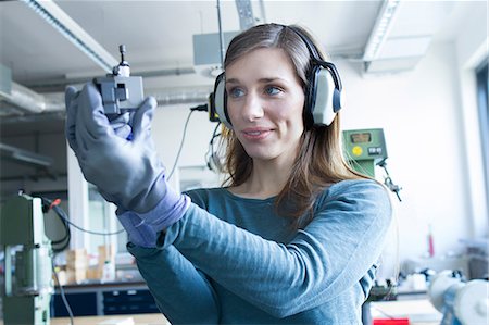 Woman in workshop wearing ear defenders operating machine smiling Stock Photo - Premium Royalty-Free, Code: 649-08549374