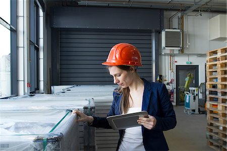 Woman in warehouse wearing hard hat looking holding digital tablet checking stock Stock Photo - Premium Royalty-Free, Code: 649-08549376