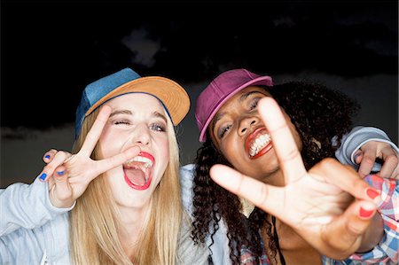 simsearch:649-08543004,k - Young woman wearing baseball cap arm around friend looking at camera doing peace sign Fotografie stock - Premium Royalty-Free, Codice: 649-08543006