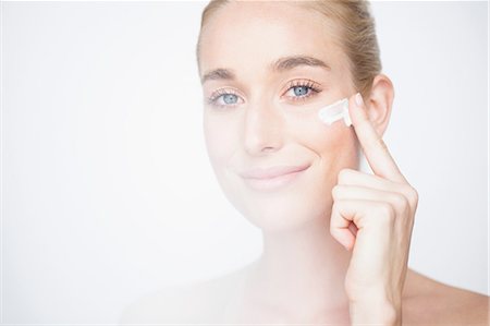 simsearch:614-06442343,k - Bare shouldered woman rubbing face cream into cheek looking at camera smiling Stock Photo - Premium Royalty-Free, Code: 649-08543059