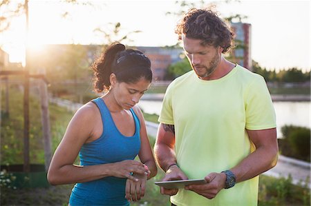 Male personal trainer and woman checking watch and digital tablet at riverside Stock Photo - Premium Royalty-Free, Code: 649-08543352