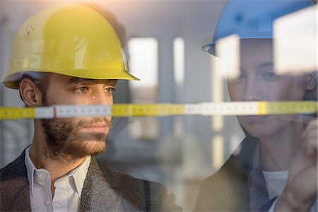 Young businessman and woman wearing hard hats measuring window in new office Stock Photo - Premium Royalty-Free, Code: 649-08543698