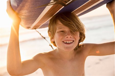 Boy carrying surfboard over head smiling Stock Photo - Premium Royalty-Free, Code: 649-08543789