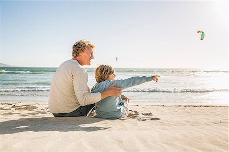 Father and son sitting on beach looking away pointing Stock Photo - Premium Royalty-Free, Code: 649-08543795