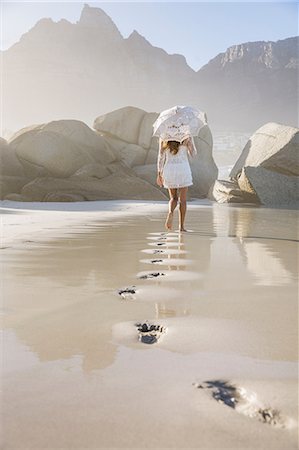 simsearch:649-03772061,k - Footprints and rear view of woman on beach wearing short white dress holding umbrella Photographie de stock - Premium Libres de Droits, Code: 649-08543856